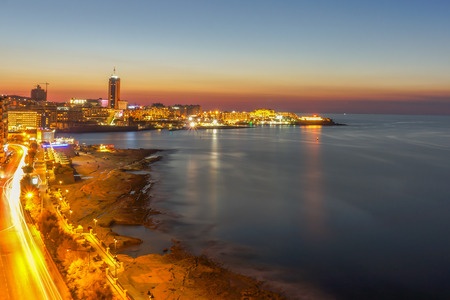 A long exposure photograph taken of the stunning waterfront in Silema, Malta. Light trails are created by cars moving up and down the road.の写真素材