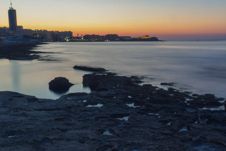 A long exposure photograph of the waterfront in Silema, Malta. The areas of St Julians and Paceville can be seen in the background as the sun sets.の写真素材