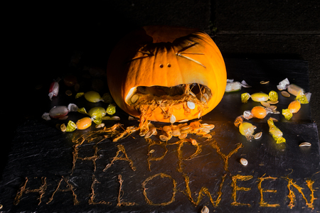 A carved pumpkin looks to be vomitting the phrase HAPPY HALLOWEEN from the pulp surrounded by treatsの写真素材