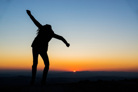 A young woman shows joyous gestures and dances in the setting sun of Dartmoor, United Kingdom.の写真素材