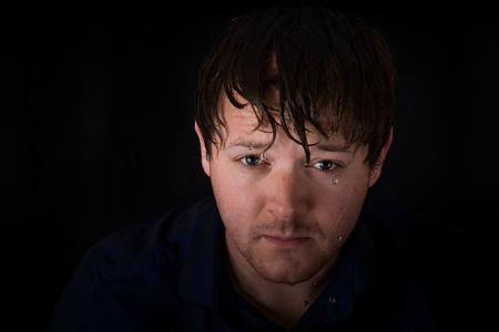 A young male looks at the camera with wet hair and water dripping in front of his face.の写真素材