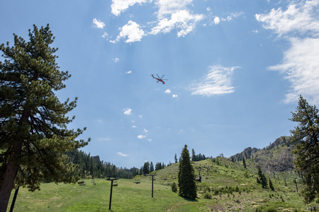 Industrial helicopter with trailing cable and hook in the mountains.  Tall pine trees and light rays lead to the helicopter.  Room for copy or added banner in the sky if needed.の写真素材
