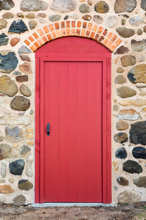 Bright red arched door set in an old field stone wall.  Lots of texture and color.の写真素材
