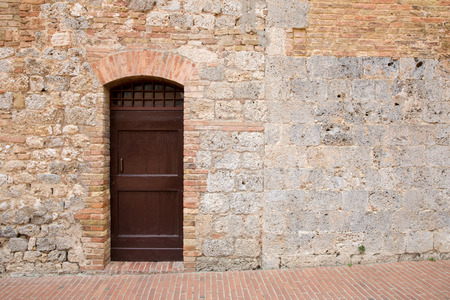 Brown door in a medieval stone and brick wall in the Tuscan village of San Gimignano, Italy.  Copy space to right of door if needed.の写真素材