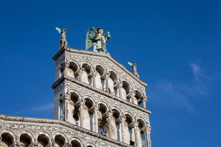 Statue of St. Michael the Archangel perched atop the Church of San Michele in the Tuscan village of Lucca, Italy.  Sculpture has blue eyes and wings.  The ornate facade dates to the 13th century.の写真素材