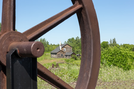 Old abandoned house viewed through a section of a rusty wheel.  Selective focus on the house.  Part of an abandoned copper mine that is now a Historic National Park in Upper Michigan.の写真素材