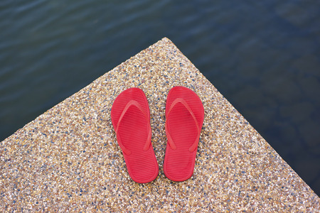 pair of red comfortable slipper placed lake side of stony floorの写真素材