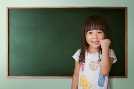 Cute little girl cheering on a background of black school boardの写真素材