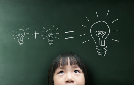 Little girl with light bulb on the blackboard background.の写真素材