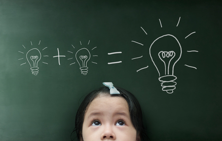 Little girl with light bulb on the blackboard background.の写真素材