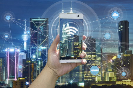 Hand holding white phone with city scape and internet network connection conceptの写真素材