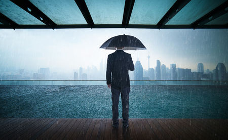 Businessman hold umbrella stand on rooftop ,raining day with city skyline view , risk and crisis concept .の写真素材
