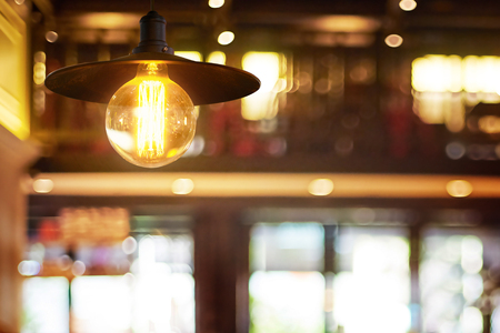 Hanging retro light lamp decor glowing in out of focus restaurant interior background .の写真素材