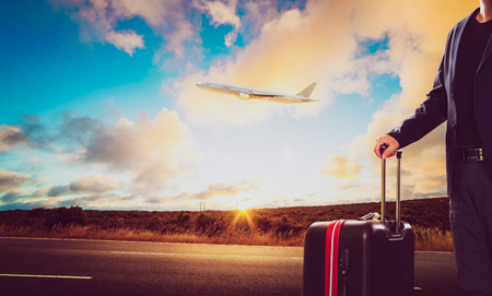 Business man with traveling luggage standing against landscape scene and passenger jet plane flying over sky .の写真素材