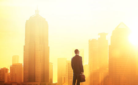 Young smart businessman looking at large city center. Concept of success and appreciation. Standing in front of the spectacular skyline with crowded corporate skyscrapers.の写真素材