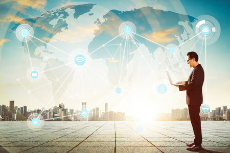 Businessman using laptop with smart city and wireless communication network background , evening scene .の写真素材