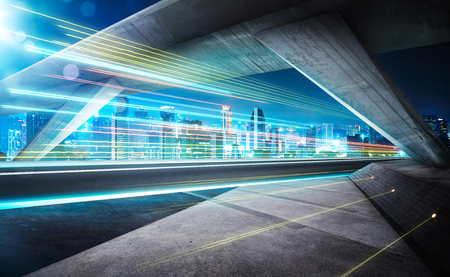 Empty asphalt road under the bridge during the night with light trails and beautiful city skyline background .の写真素材