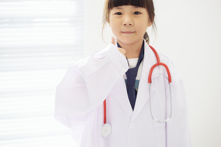 Portrait of little girl dressed as a doctor with a stethoscope and hands with thumbs up .の写真素材