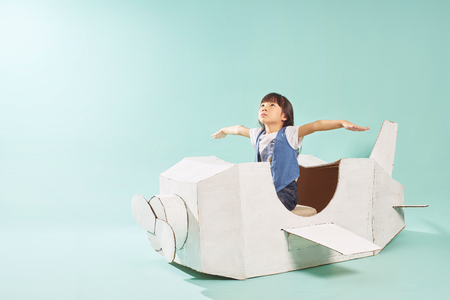 Little cute girl playing with a cardboard airplane. White retro style cardboard airplane on mint green background . Childhood dream imagination concept .の写真素材