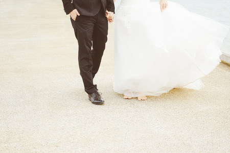 Just married loving couple in wedding dress and suit walking and holding hands on a stone jetty. Closeup half body .の写真素材