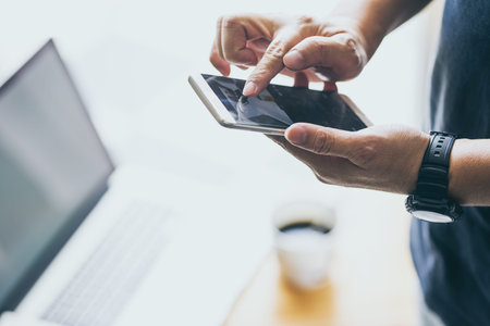Smartphone in young man hand with blur laptop and coffee background .