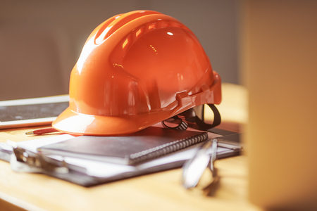 Laptop ,glasses, note book ,phone ,blueprint and orange safety helmet stacking on table at construction site for Engineer, foreman and worker , selective focusing .の写真素材