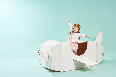 Little cute girl playing with a cardboard airplane. White retro style cardboard airplane on mint green background . Childhood dream imagination concept .の写真素材