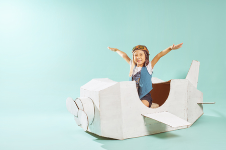 Little cute girl playing with a cardboard airplane. White retro style cardboard airplane on mint green background . Childhood dream imagination concept .の写真素材