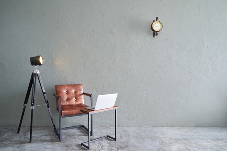 Modern living room with brown iron chair , clock ,tea table,laptop and lamp stand. cement floor and concrete wall ,Interior design with Loft style .の写真素材