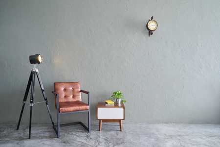 Modern living room with iron brown relax chair ,green plant , lamp stand , wooden tea table and clock. cement floor and concrete wall , Interior design with Loft style .の写真素材