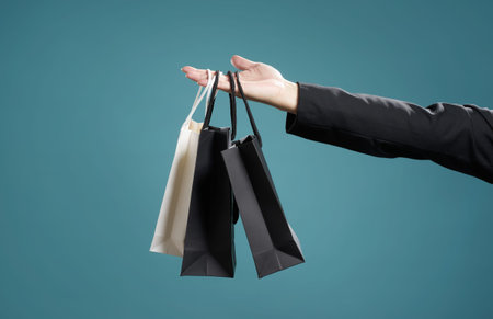 Close up of man's hand with shopping bags, isolated on light blue background.