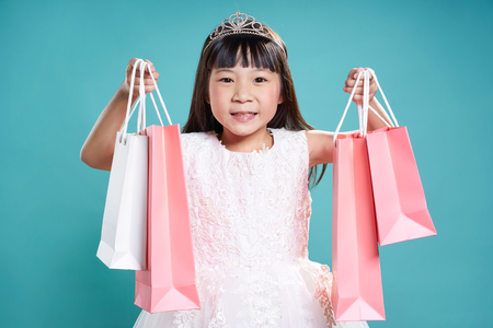 Close up portrait of asian little happy girl with shopping bags , isolated on light blue background .の写真素材