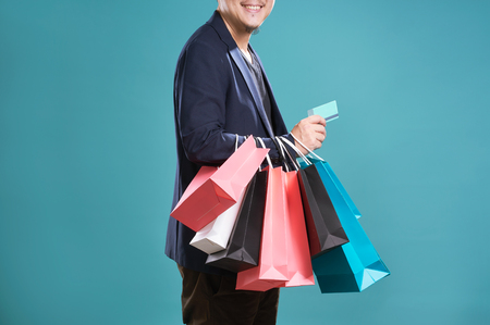 Close up of man  in suit holding credit card with shopping bags , isolated on light blue background .の写真素材