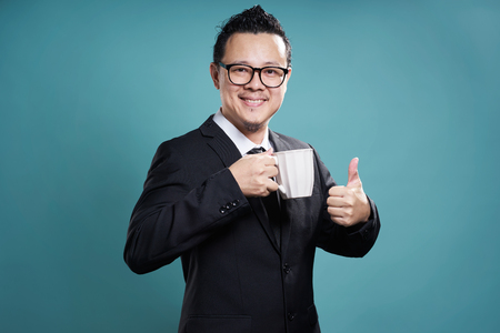 Businessman in suit smile and enjoy cup of coffee with thumb up gesture.の写真素材