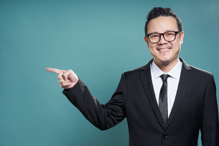 Portrait of asian businessman smile and points with finger to camera left on vintage blue background .の写真素材