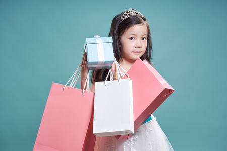 Portrait of little asian beautiful girl holding  present box and shopping bag on vintage blue background .の写真素材