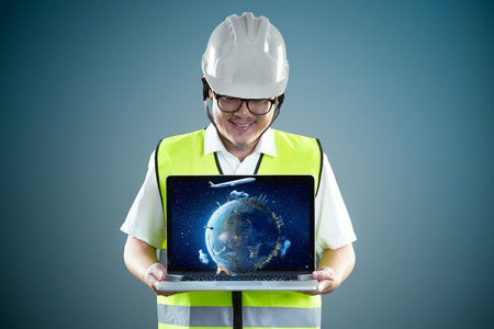 Young engineer in safety helmet and using laptop with virtual reality earth to show client something.の写真素材