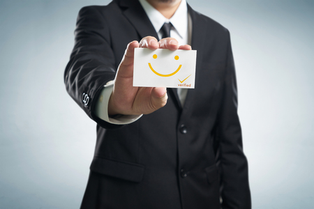Businessman hand showing business card with smile icon .Concept of happy and satisfaction customer experience .の写真素材