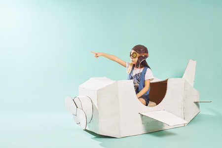 Little cute girl playing with a cardboard airplane. White retro style cardboard airplane on mint green background . Childhood dream imagination concept .の写真素材
