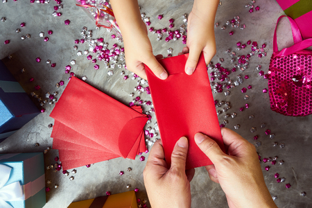 Close up hands of parent giving a red envelope or money red packet to child  .  Chinese new year and Lunar new year festival concept background . Top view .の写真素材