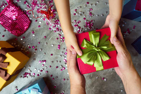 Close up hands of parent giving a Christmas gift to child with colorful gift box and little star craft background .  Cement texture desktop top view .の写真素材