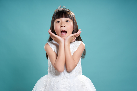 Portrait of little surprise asian princess girl in silver crown and white dress isolated on vintage green background .の写真素材