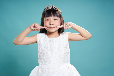 Portrait of little smile asian princess girl in silver crown and white dress isolated on vintage green background .の写真素材