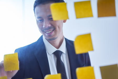 Asian businessman stand in glasses board with stickers and writing ideal , brainstorming concept .の写真素材