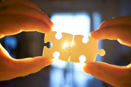 Young businessman trying to connect couple puzzle piece with sun flare and blur background,symbol of association and connection. business strategy.の写真素材