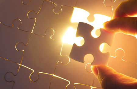 Young businessman trying to put back missing jigsaw puzzle piece with light golden glow effect . Business strategy concept .の写真素材