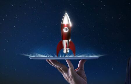 Waiter hand holding an empty digital tablet with Metallic red antique style rocket space ship , Startup creative concept .の写真素材