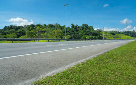 Perspective view of empty highway road with railing,green hill,blue sky and light polesの写真素材