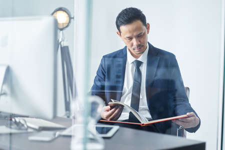 Young Asian Businessman reading book in officeの写真素材