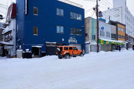 Hokkaido, Japan - December 19, 2022 : A stylish orange Jeep is parked on the snow-covered street in Hokkaidoのeditorial素材